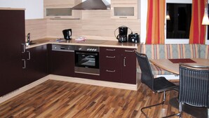 Une cuisine compacte équipée d’un four encastré, d’une machine à café et d’un four à micro-ondes. Un coin repas avec une table et des chaises est également disponible.