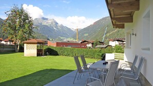 Une terrasse avec une table et des chaises, un petit abri de jardin et une vue sur les montagnes et les bâtiments en arrière-plan.
