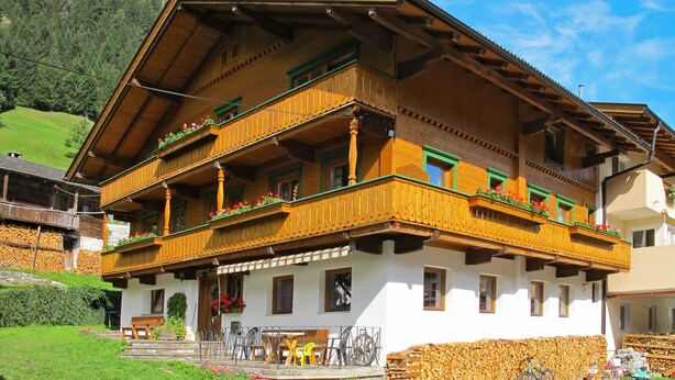 Un chalet traditionnel en bois, doté d’un balcon, d’un mur en pierre et surplombant un paysage montagneux.