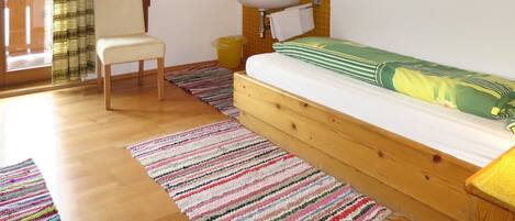 Quarto com cama de madeira, uma cadeira, pia pequena e janela com cortinas.