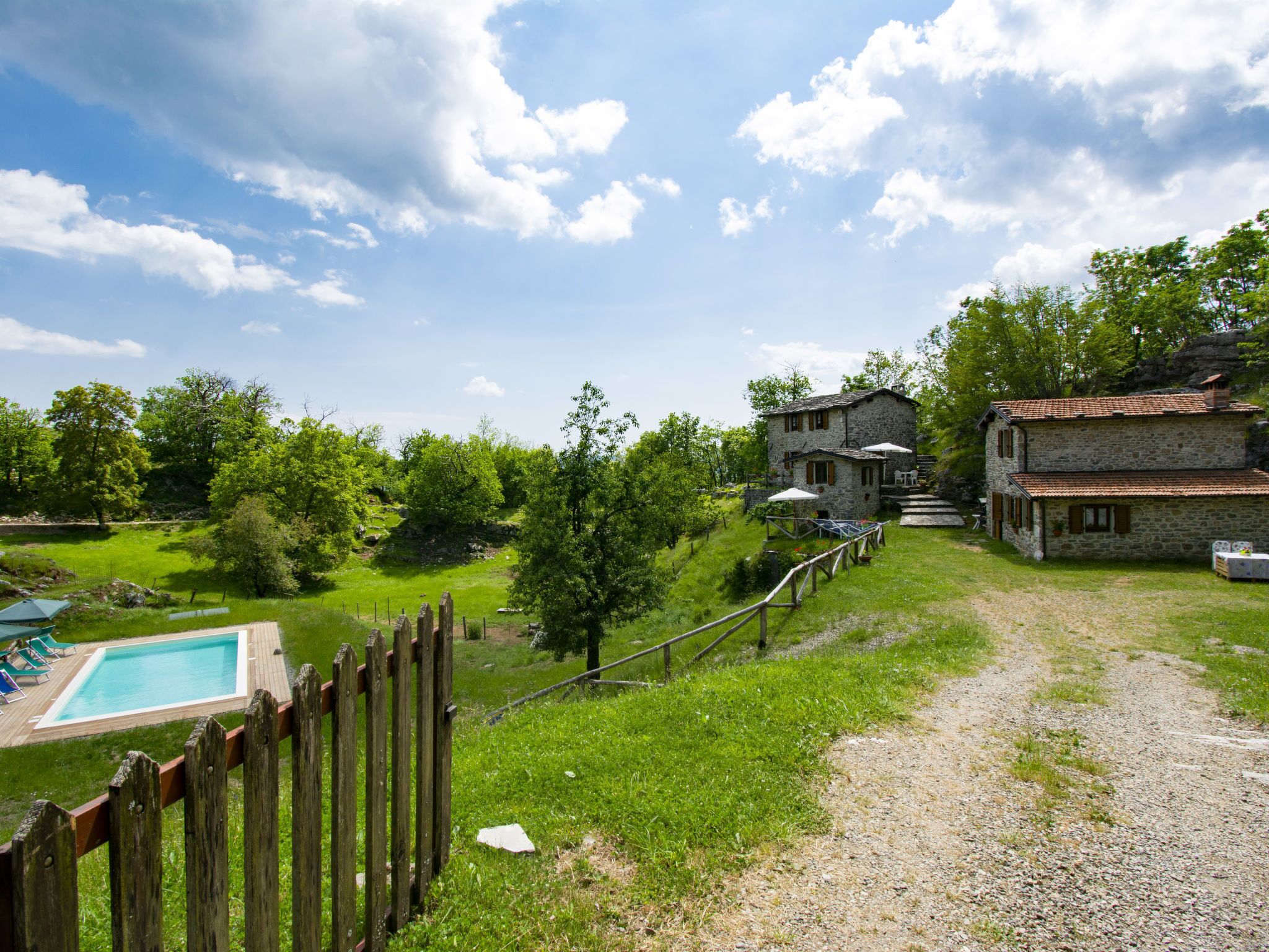 Une maison en pierre avec une piscine, entourée d’une clôture en bois et d’une végétation luxuriante.