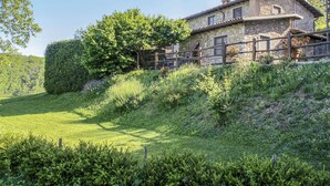 A stone house with a wooden fence, surrounded by lush greenery and a clear sky. - Le Bore (CNG122) by Interhome (Castelnuovo di Garfagnana)