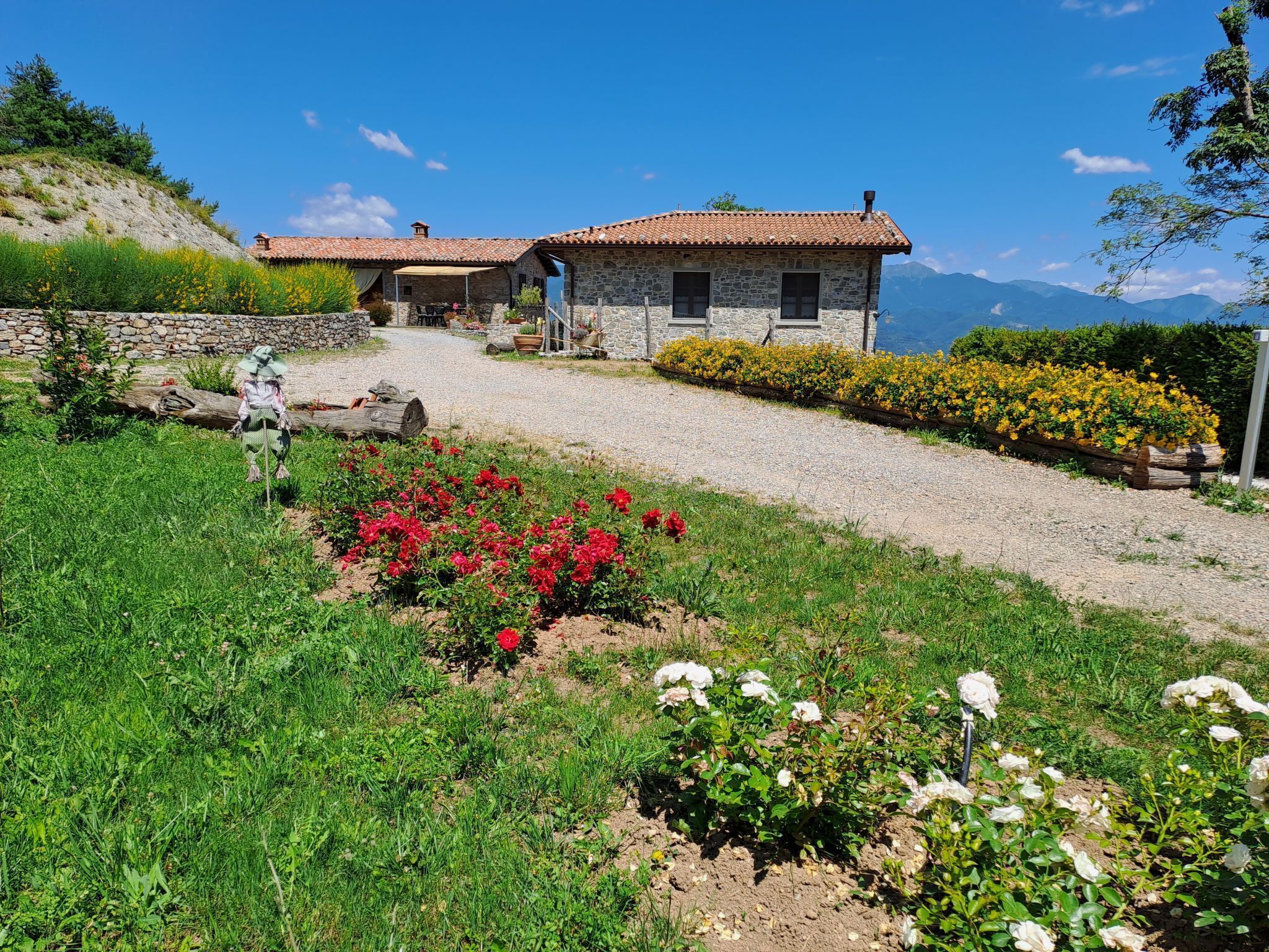 A stone house with a tiled roof, surrounded by a gravel driveway and flower beds.