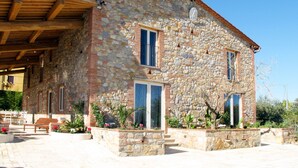 A stone building with a sloped roof, wooden beams, and a covered patio area with benches.