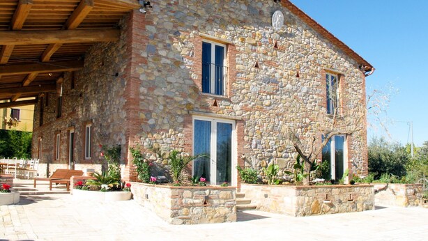 A stone building with a sloped roof, wooden beams, and a covered patio area with benches.