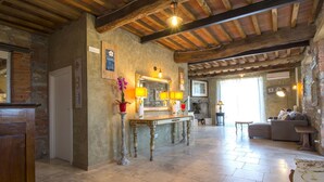 A rustic interior with exposed wooden beams, a stone fireplace, and a tiled floor.