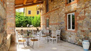 An outdoor patio with stone walls, wooden beams, and white furniture.