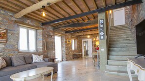 A spacious living area with a stone wall, a wooden ceiling, and a staircase leading to an upper floor.