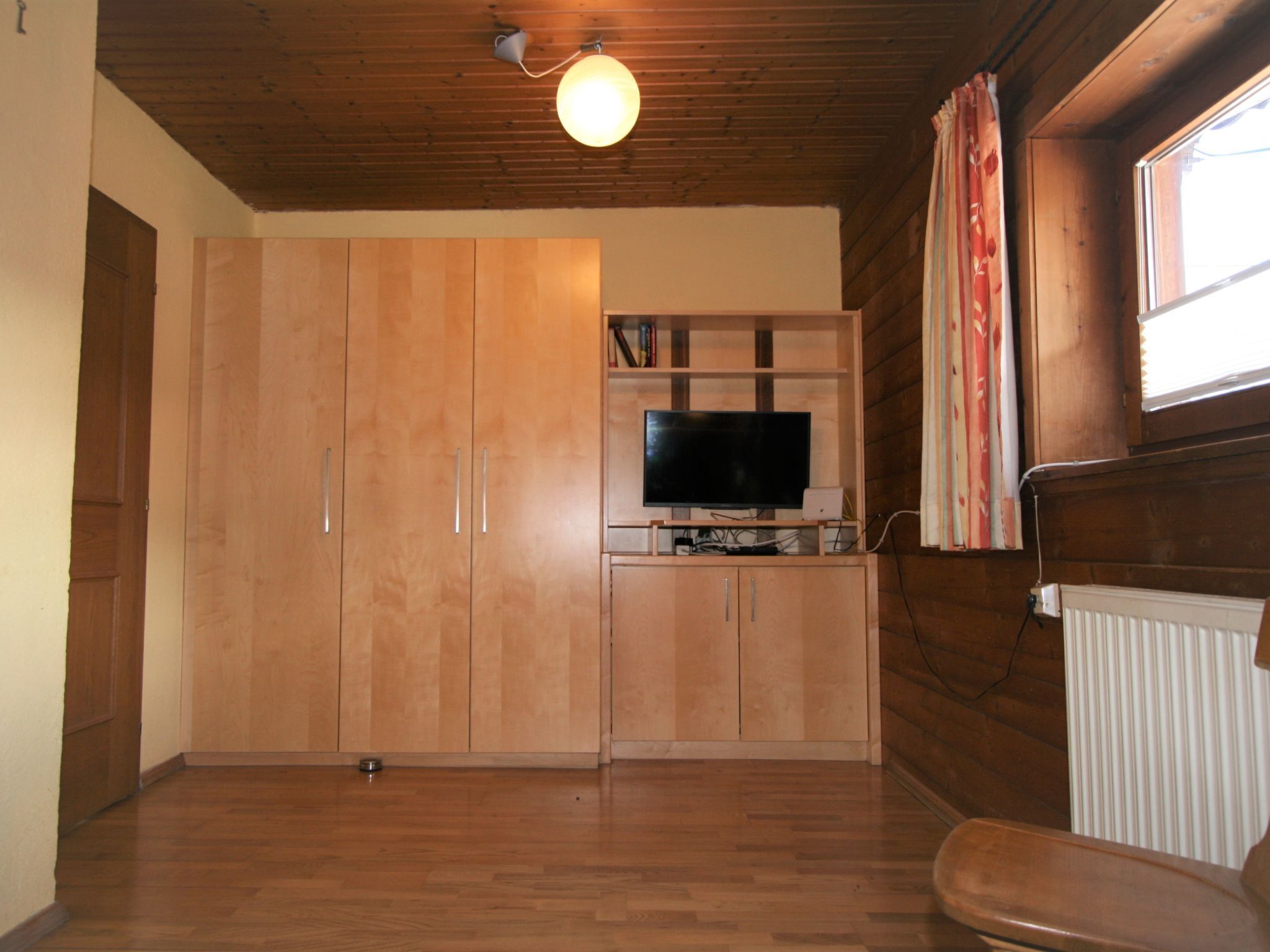 A room with wooden cabinets, a television on a stand, and a window with curtains.