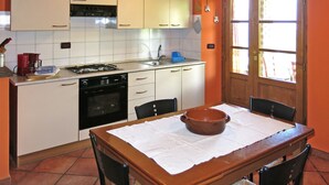 Eine Küche mit weißen Schränken, einem Herd und einem Spülbecken. Ein Holztisch mit Stühlen und ein großes Fenster mit Vorhängen sind ebenfalls vorhanden.