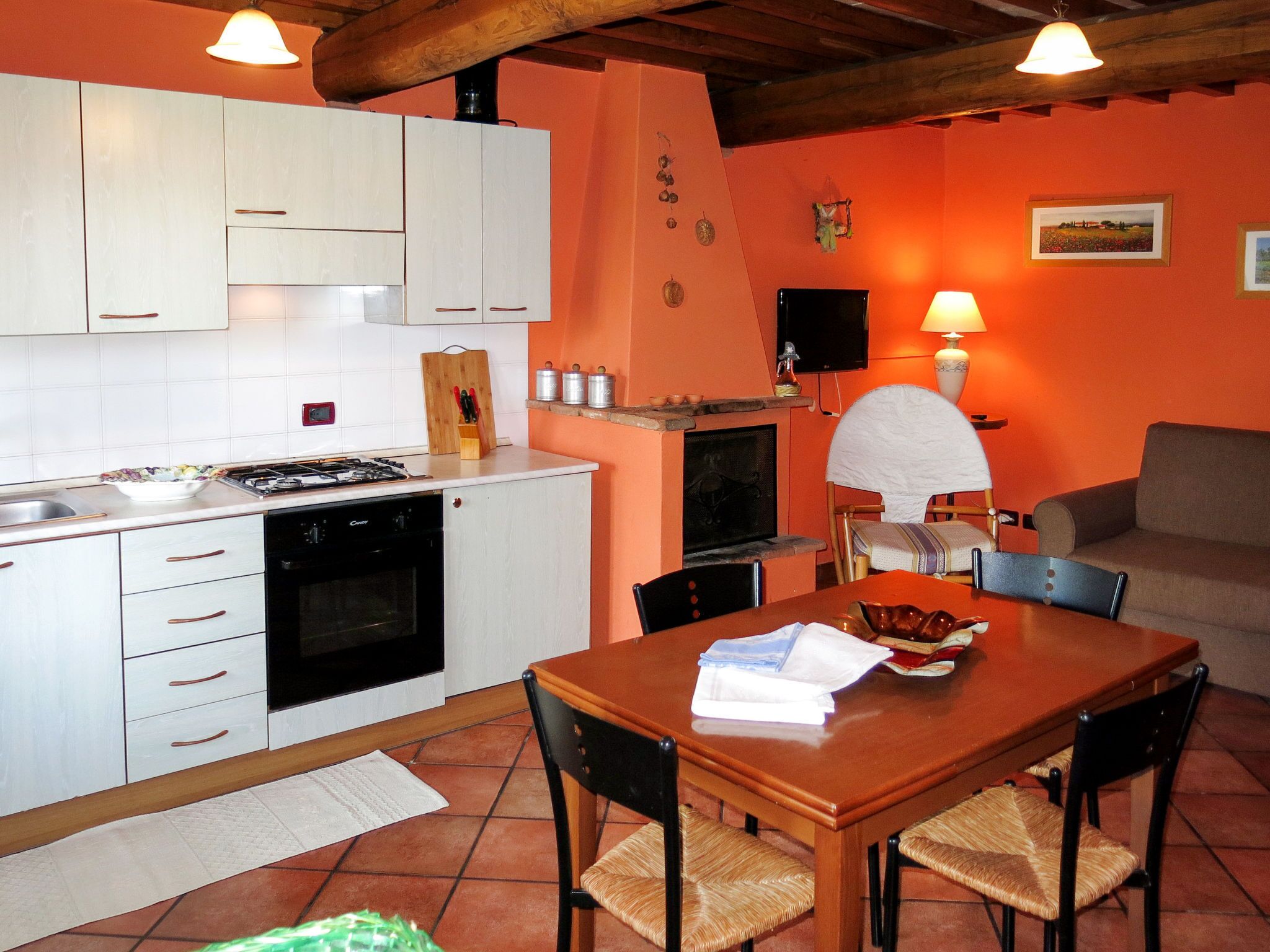 Una cocina compacta con armarios blancos, una estufa y un lavavajillas. Hay una mesa de comedor con sillas y un sofá en la zona de estar contigua.