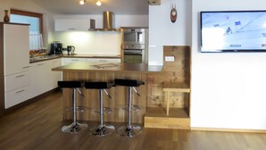 A modern kitchen with a wooden island, bar stools, stainless steel appliances, and a TV mounted on the wall. - Apart Vorwies by Interhome (Fügen)
