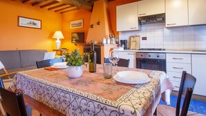 Uma área de jantar aconchegante com uma mesa posta para dois, um sofá e uma cozinha ao fundo.
