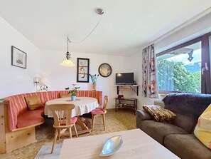 A living room with a sofa, a dining table with chairs, a TV on a stand, and a window with curtains. - Höllwarth by Interhome (Fügen)
