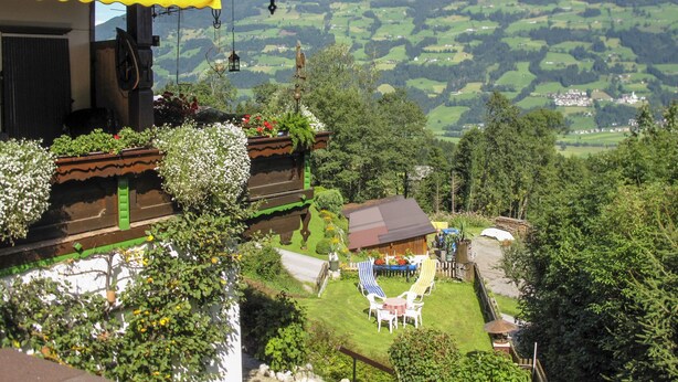 A view of a mountainous landscape with a house featuring a balcony with plants, a small garden, and outdoor seating.