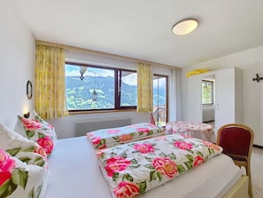 A bedroom with two beds, a window with a mountain view, a radiator, and a chair. - Höllwarth by Interhome (Fügen)