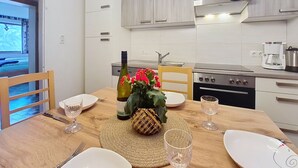 A modern kitchen with a dining table set for two, a coffee maker, and a bottle of wine.
