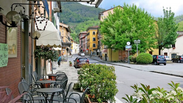 A street view with outdoor seating, a mountain backdrop, and parked cars. - Natalie (BLU170) by Interhome (Bagni di Lucca)