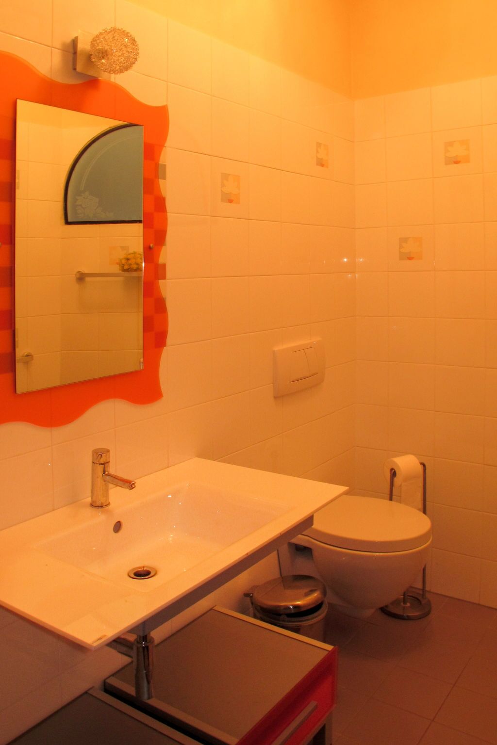 A bathroom with a white sink, a mirror, a toilet, and a trash bin.