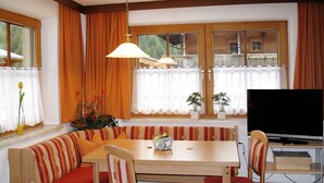 A cozy dining area with a wooden table, red cushioned benches, and a television on a stand. - Theresia by Interhome (Alpbach)