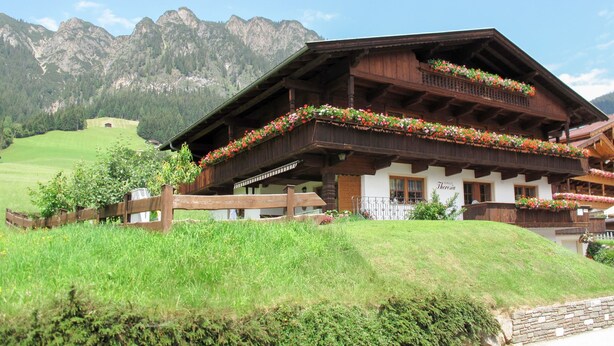A traditional Alpine chalet with a wooden balcony adorned with flowers, set against a backdrop of mountains and a clear sky. - Theresia by Interhome (Alpbach)