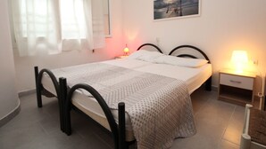 Un dormitori ordenat amb un llit, dues taules de nit, una petita taula auxiliar, una finestra amb cortines i un quadre penjat a la paret.