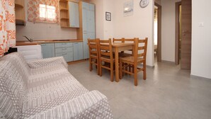 Un saló amb un sofà, una taula de dinar amb cadires, una zona de cuina amb armaris i un rellotge a la paret.