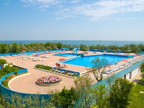 Ein Resort mit einem großen Schwimmbecken, Liegestühlen und Blick aufs Meer.
