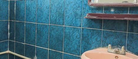 A bathroom with blue tiles, a pink sink, and a window.