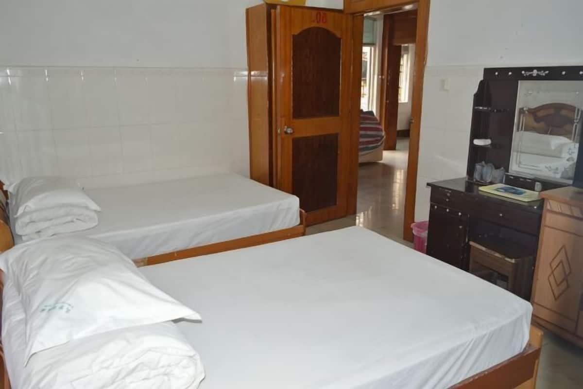 A room with two single beds, a wooden wardrobe, a desk with a mirror, and a door leading to another room.