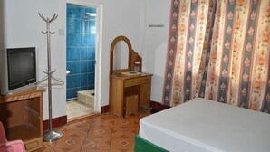 Habitación de hotel con cama, televisor, cómoda de madera, espejo y baño con azulejos azules.