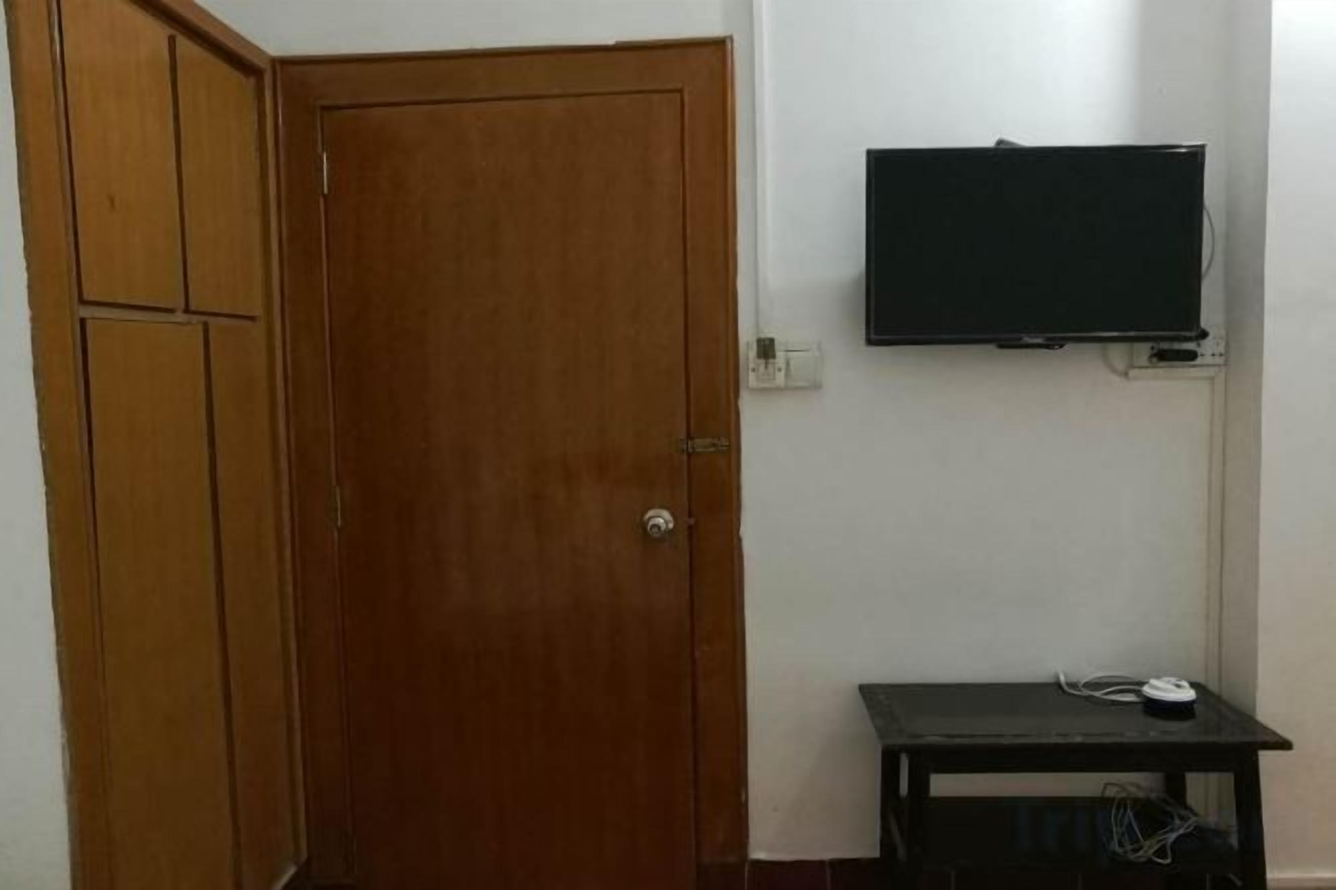 Une pièce avec une porte en bois, un téléviseur fixé au mur et une petite table sur laquelle se trouve une télécommande.