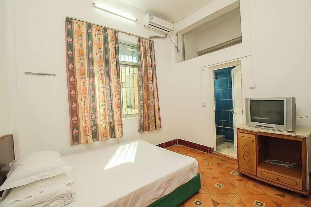 A room with a bed, a television on a cabinet, a window with curtains, and an air conditioning unit.