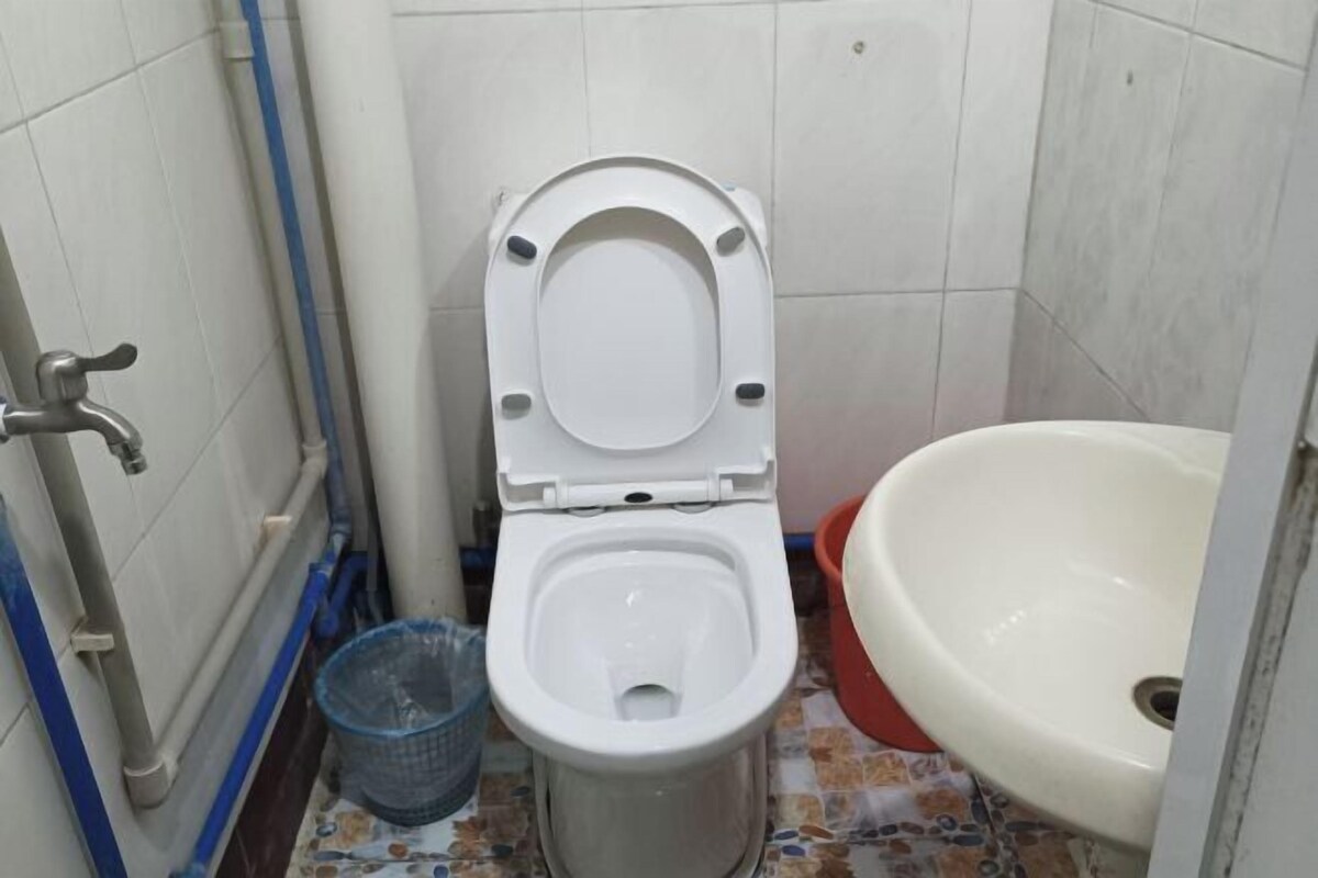 A small bathroom with a toilet, a sink, and a blue trash bin.