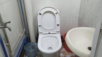 Een kleine badkamer met een toilet, een wastafel en een blauwe prullenbak.