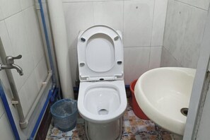 A small bathroom with a toilet, a sink, and a blue trash bin. - Qionghai Boyi Fanjiale Hotel (Qionghai)
