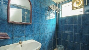 Un baño con azulejos azules, un lavamanos blanco, un espejo y una ventana con lámpara.