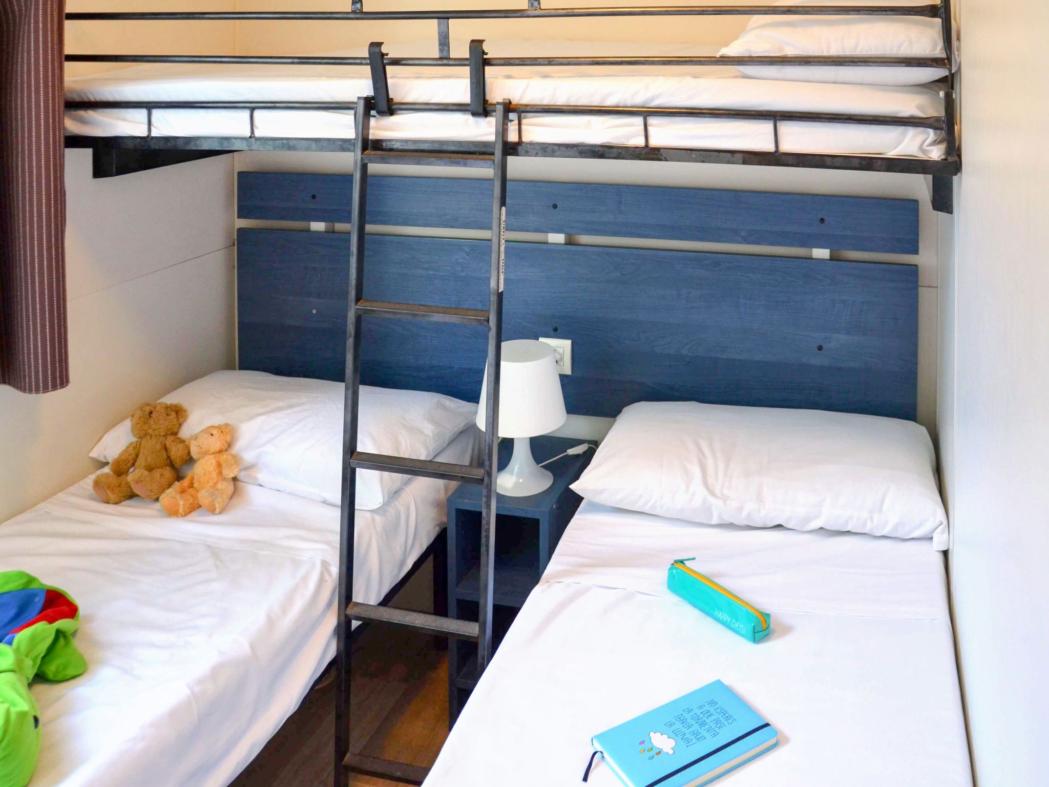 A bunk bed room with a ladder, a bedside lamp, a teddy bear, a green toy, and a notebook.