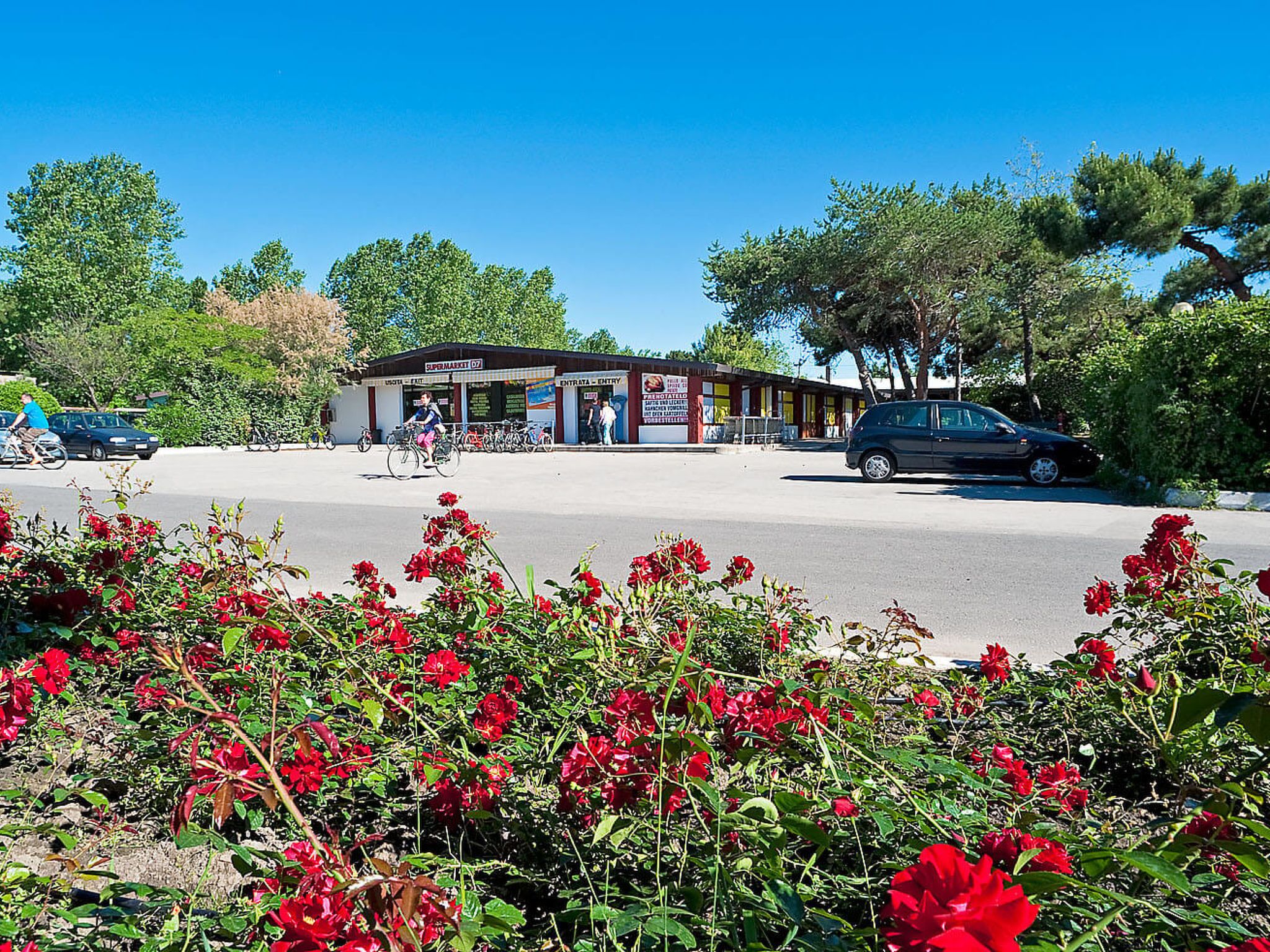 A small building with a sign reading "SUPERMARKET 07" and a parking lot with cars and bicycles.