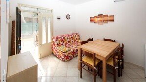 A dining area with a wooden table and chairs, a floral sofa, and a wall-mounted artwork. - Casa Debora by Interhome (Rosolina Mare)