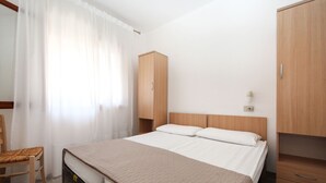 A bedroom with a bed, wooden wardrobe, and a chair. - Casa Debora by Interhome (Rosolina Mare)