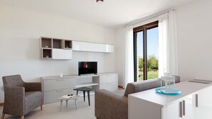 A modern living room with a sofa, a coffee table, a TV, and a dining area with a white cabinet and a blue tray. - Ca' Del Pioppo by Interhome (Cavallino)