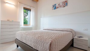 A bedroom with a bed, a nightstand, a dresser, a window, and a painting on the wall. - Ca' Del Pioppo by Interhome (Cavallino)