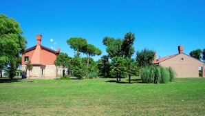 A building with a red roof and brick walls, surrounded by a grassy field and trees. - Ca' Del Pioppo by Interhome (Cavallino)