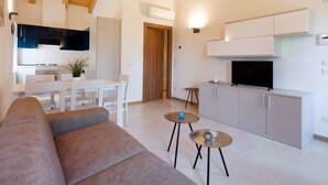 A modern living room with a sofa, two small tables, a TV, and a kitchen area with cabinets and a stove. - Ca' Del Pioppo by Interhome (Cavallino)