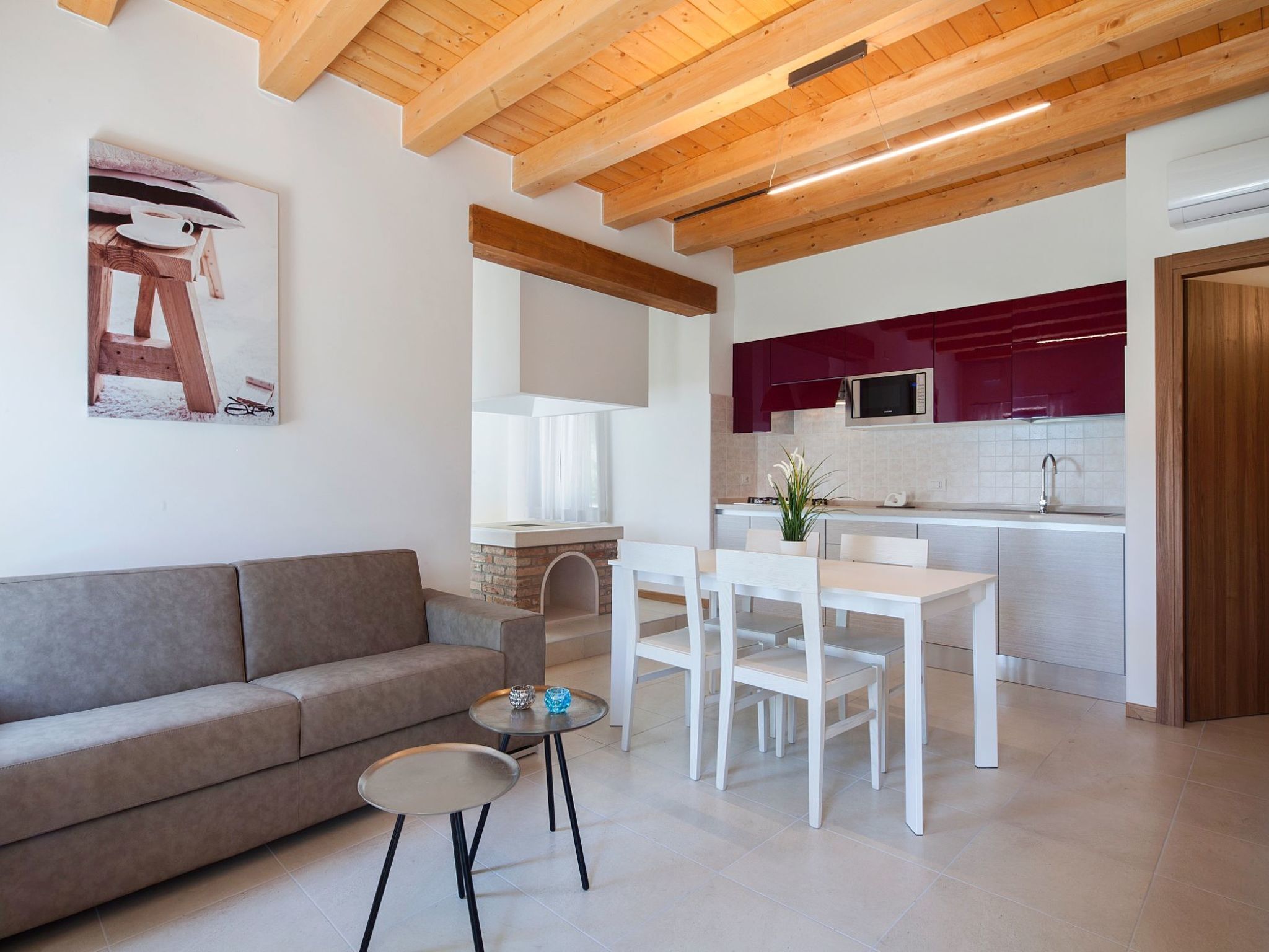 Una sala de estar moderna con un sofá, una mesa de comedor con sillas y una zona de cocina con armarios rojos y un microondas.