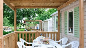 A covered outdoor dining area with a wooden deck, white plastic chairs, and a table set for four.