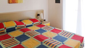 Un llit amb un llençol de colors, una taula de nit amb una làmpada i un quadre a la paret.