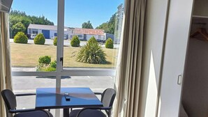 A room with a table and chairs, a window with curtains, and a view of a parking lot and buildings.