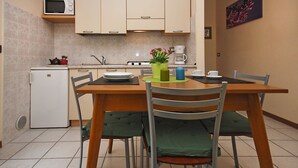 Une cuisine compacte équipée d’un four à micro-ondes, d’une cuisinière et d’un évier. On y trouve une table à manger avec des chaises, ainsi qu’un petit réfrigérateur.